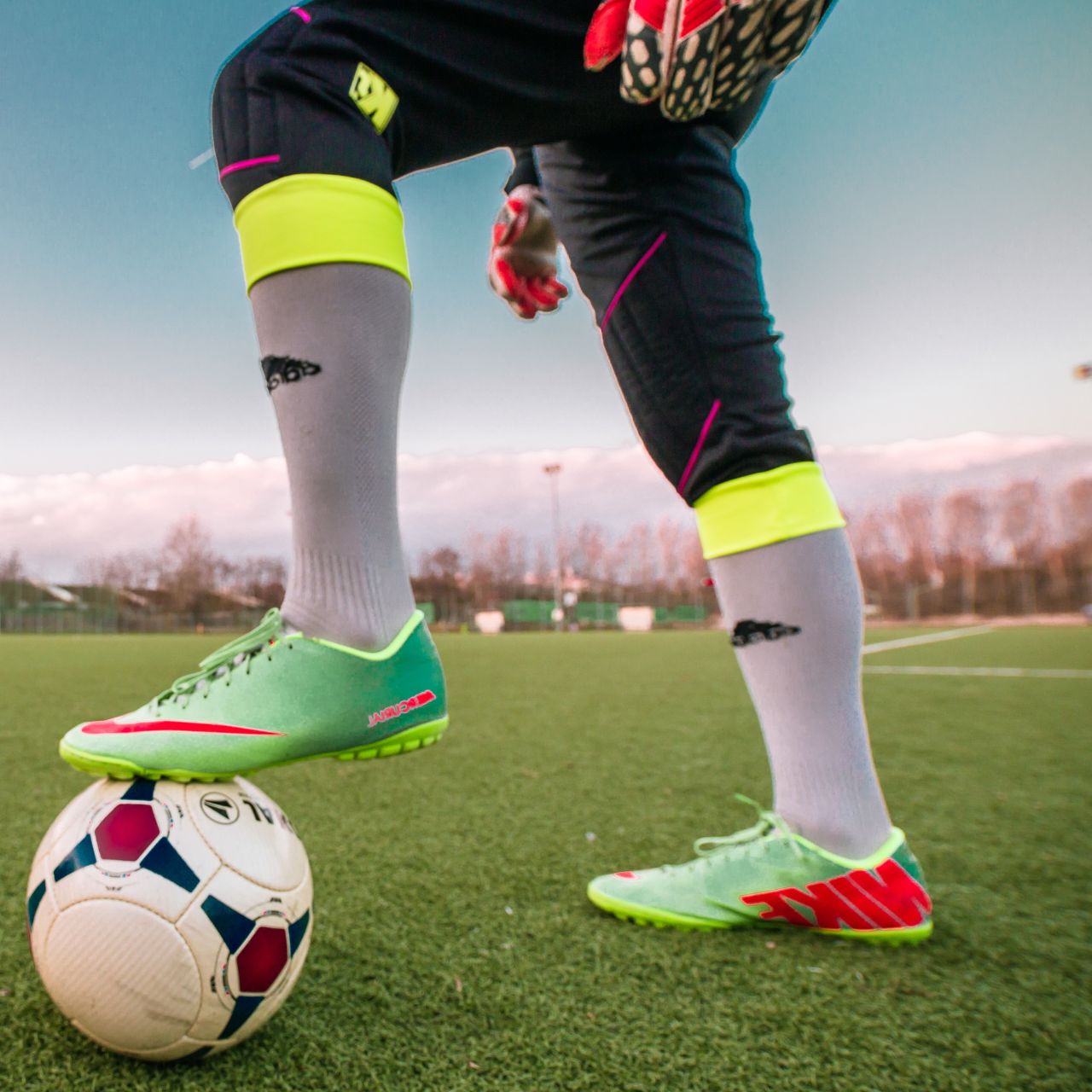 A soccer player with one foot on the ball on a sports field